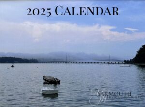 The 2025 calendar cover photo features a calm, but foggy, view of the Cousins Island bridge with a small boat in the foreground.