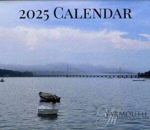 The 2025 calendar cover photo features a calm, but foggy, view of the Cousins Island bridge with a small boat in the foreground.